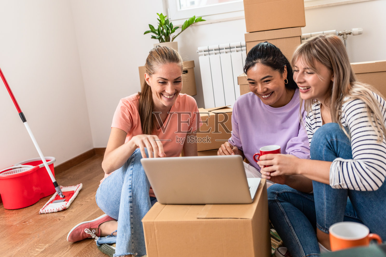 女性朋友坐在新公寓的地板上用笔记本电脑。照片摄影图片