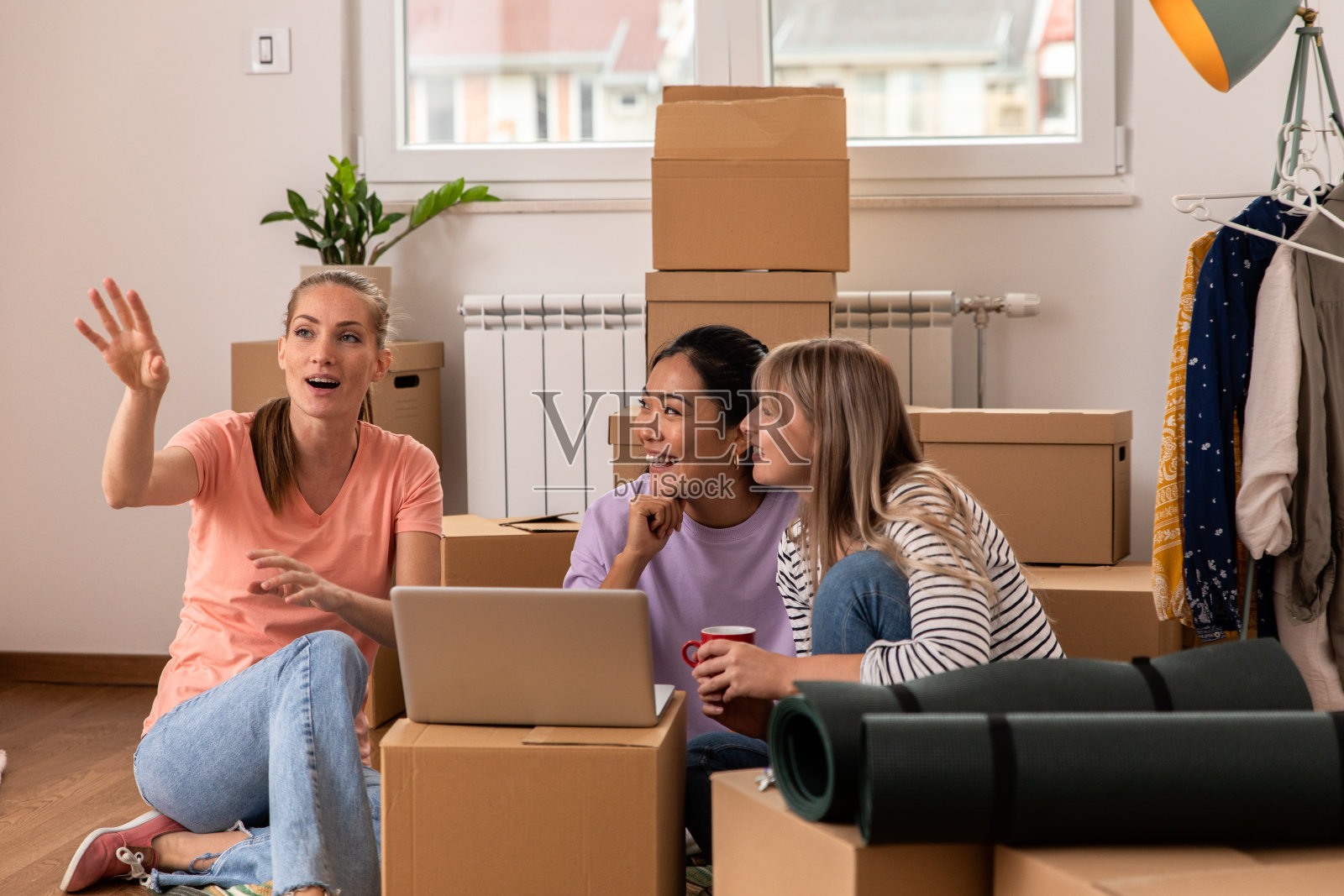 女性朋友坐在新公寓的地板上用笔记本电脑。照片摄影图片