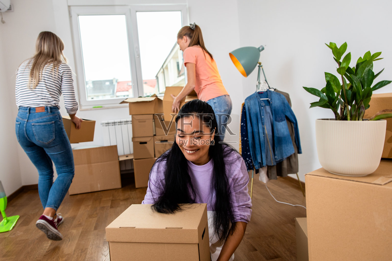 三位女性朋友扛着箱子搬进新家。照片摄影图片