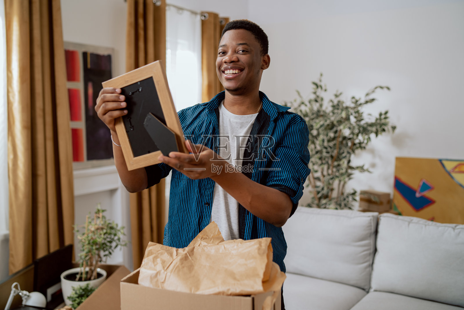 一个男人在搬到新公寓后打扫客厅，打开纸箱里的东西，男孩发现一个相框里有一张他童年时的照片，他震惊的高兴，喜悦的看着照片摄影图片
