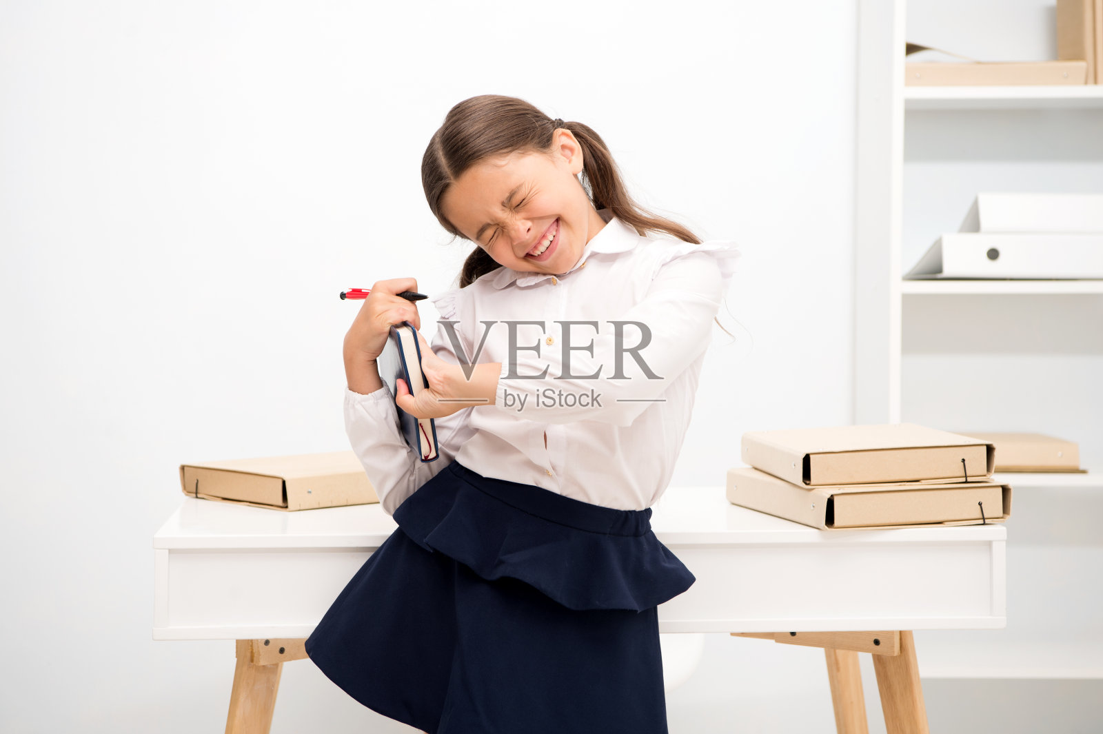 儿童校服做运动拉伸提高生产力。锻炼以保持活力。主动中断在教育过程中的作用。女孩拿着书，同时伸展白色的内部照片摄影图片