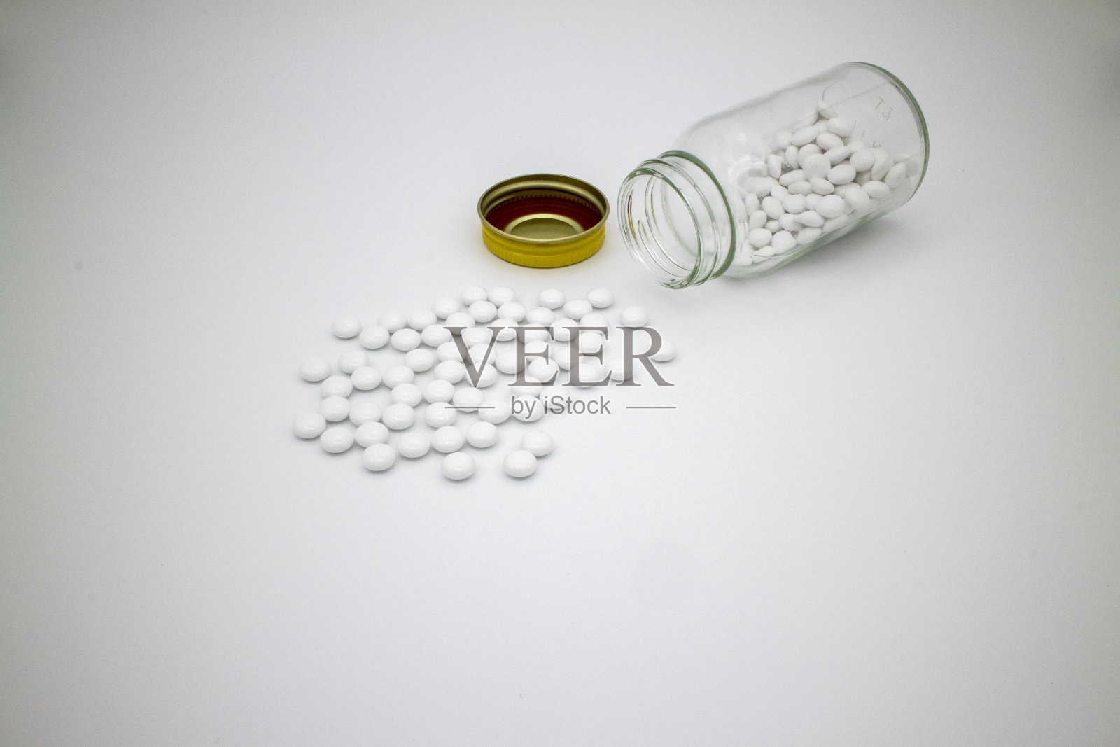 白色的药片从玻璃瓶中扩散出来，在白色的表面上照片摄影图片