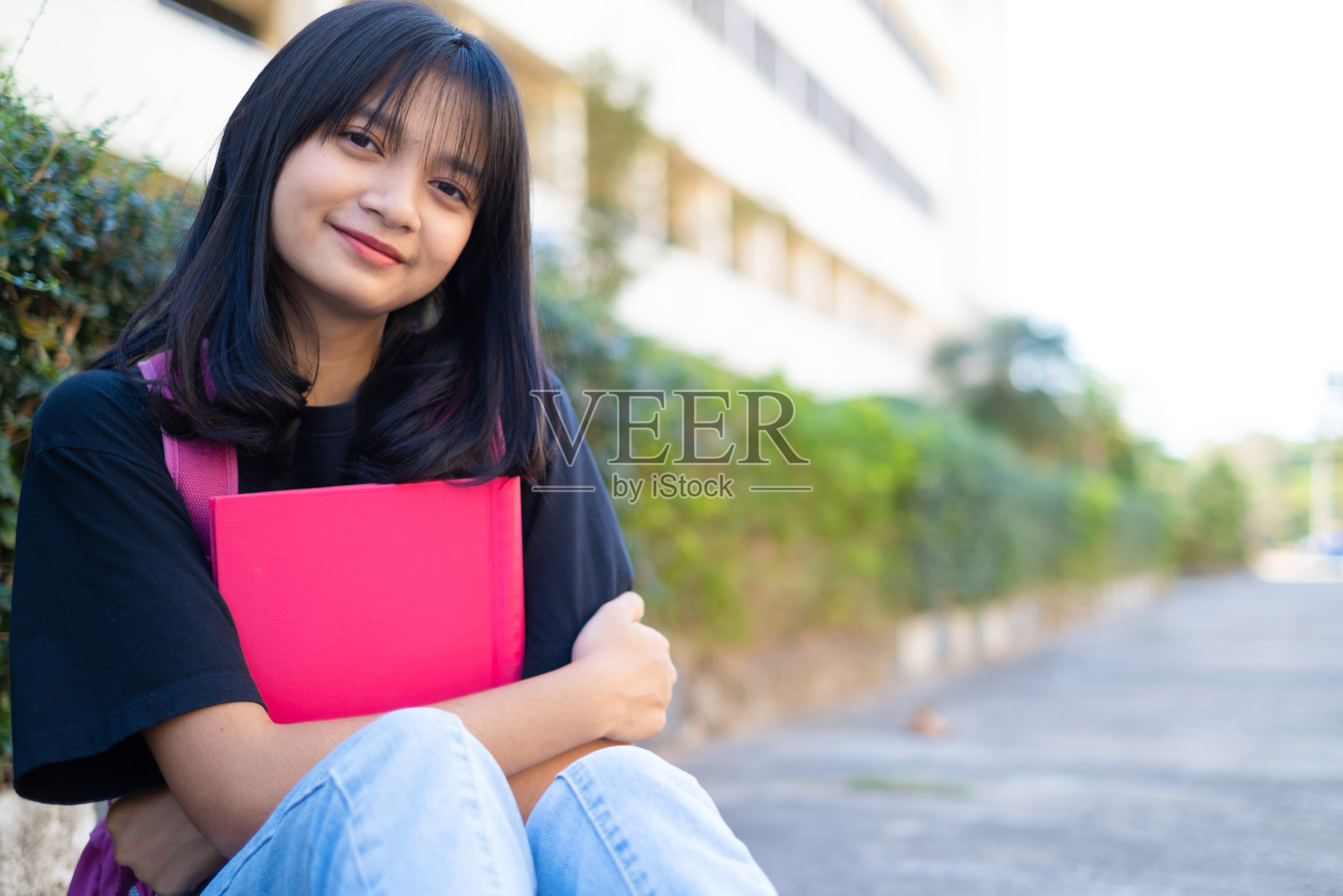 学生年轻的女孩与粉红色的背包坐在地板上与学校的背景。照片摄影图片
