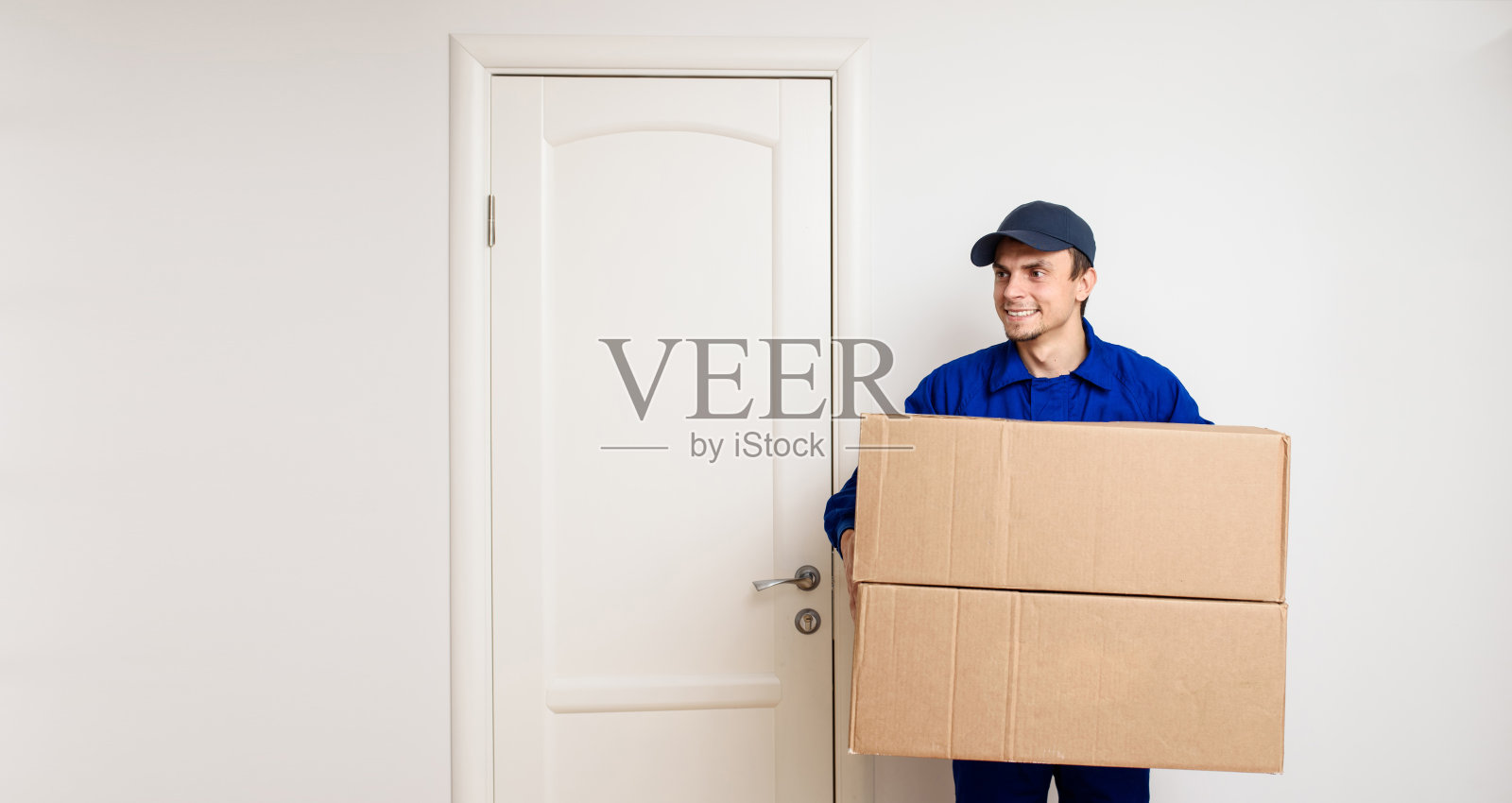 穿着蓝色制服的年轻快乐的快递员正在给客户送包裹。照片摄影图片