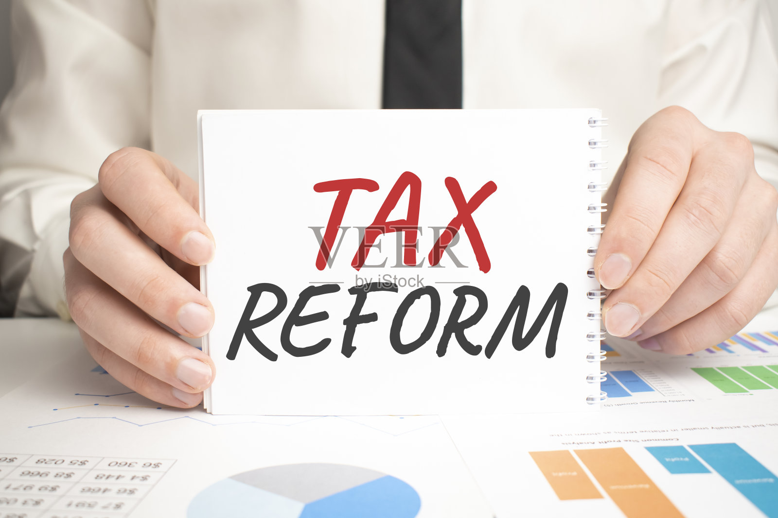 商人手持记事本，上面写着“TAX REROFM”。桌面上的财务图表。财务及经营理念。照片摄影图片