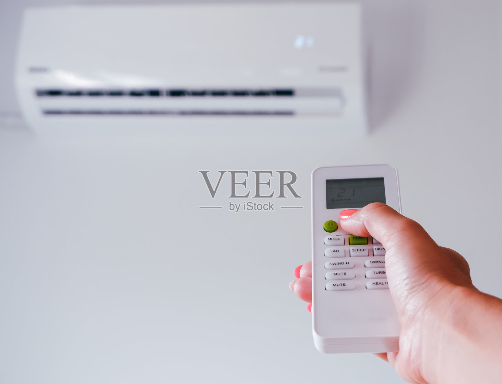 空调。一位女士手里拿着空调的遥控器。背景为壁挂式空调机组。照片摄影图片