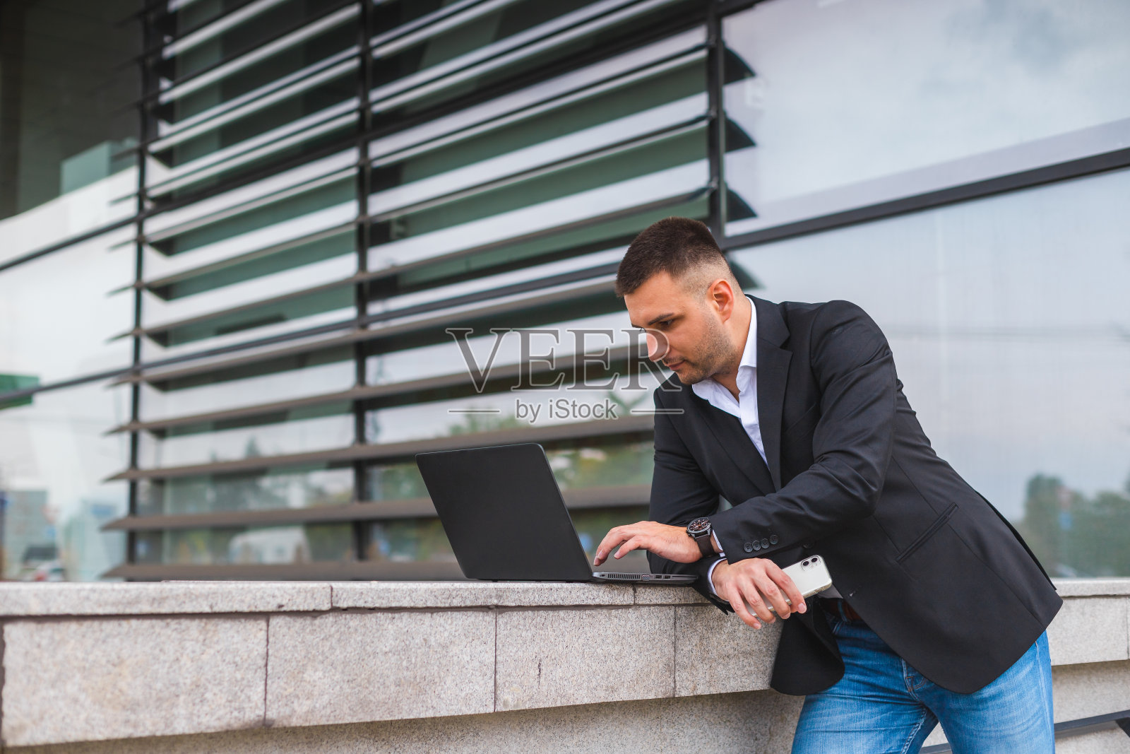 年轻英俊的白人商人，穿着黑色西装，在外面的城市场景中使用笔记本电脑照片摄影图片