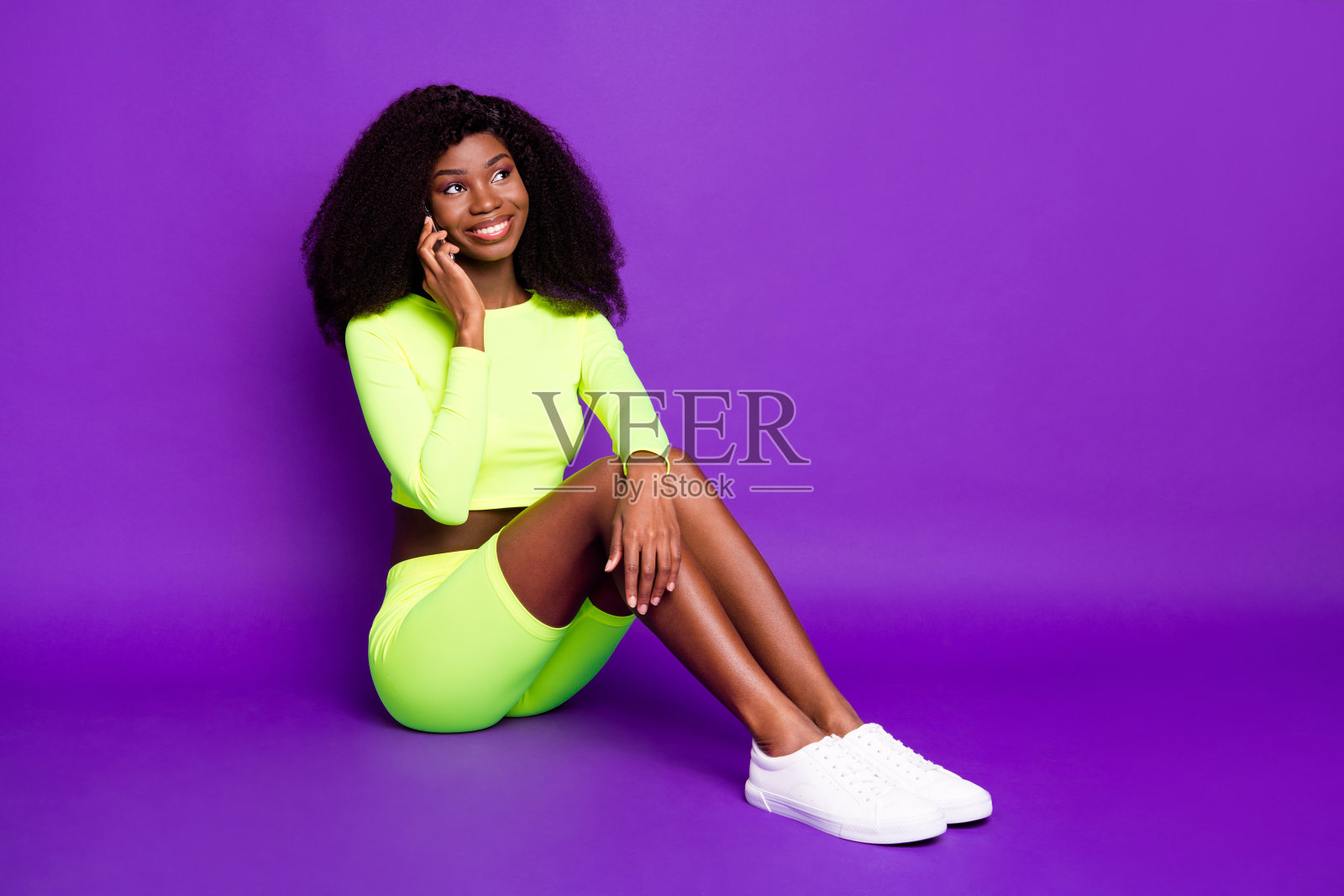 漂亮女孩的照片抱着电话沟通看空空间穿绿色衬衫短裤鞋子孤立的紫色背景照片摄影图片