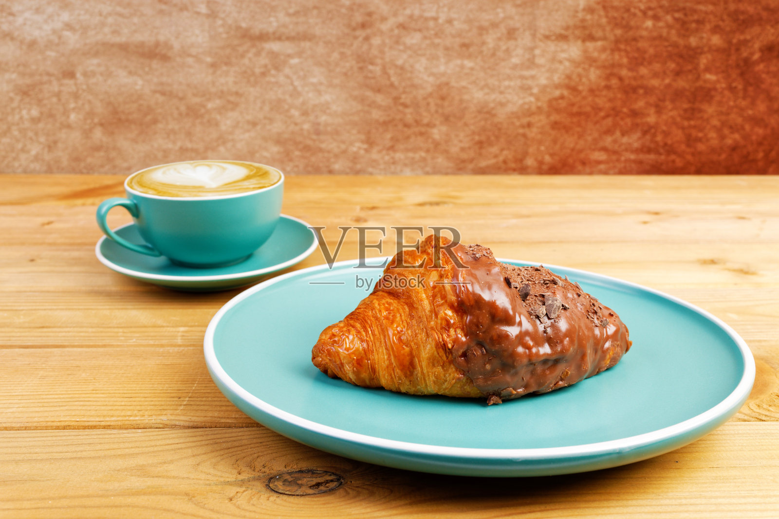 木桌上一杯卡布奇诺咖啡和巧克力羊角面包。浅的焦点。照片摄影图片