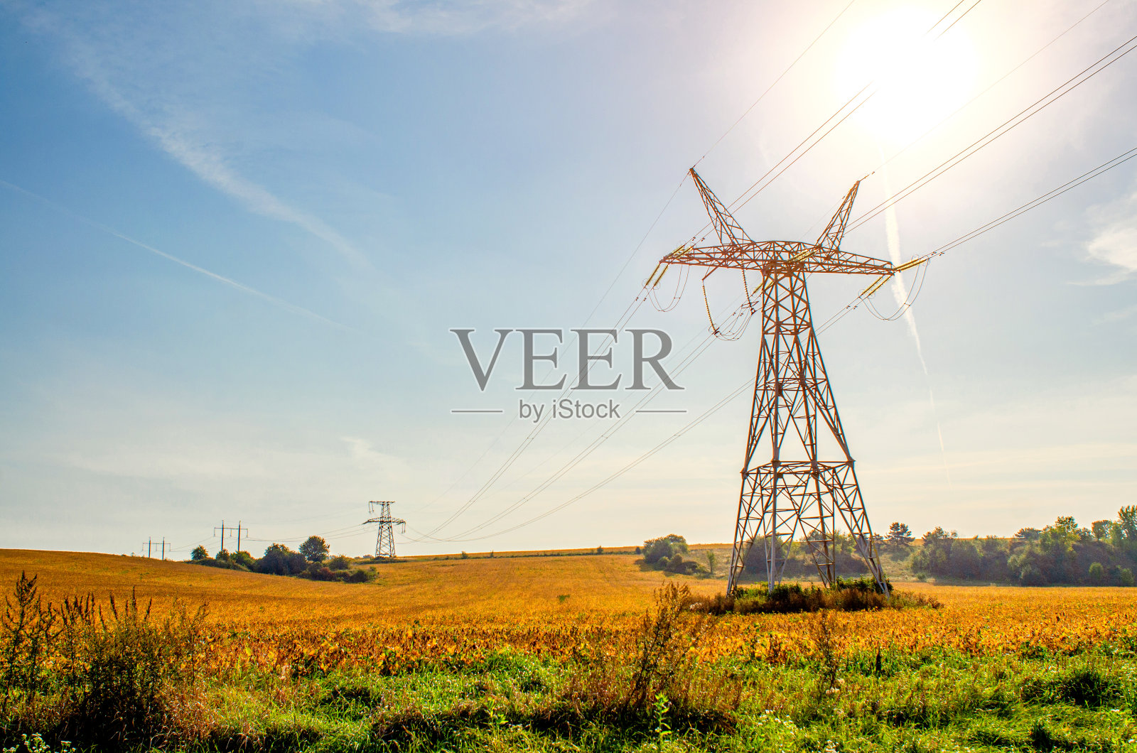 高压电线的背景是蓝天和绿色的植被。照片摄影图片