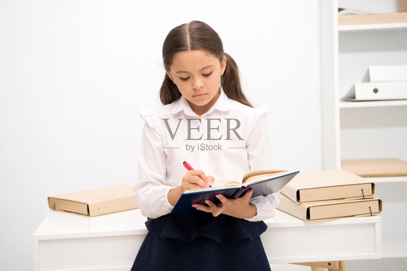 写的任务很无聊。如何让一年级学生的教育更有趣。女孩抱着书做笔记。孩子上学穿校服沉着伤心冷漠的脸写课本。对知识照片摄影图片