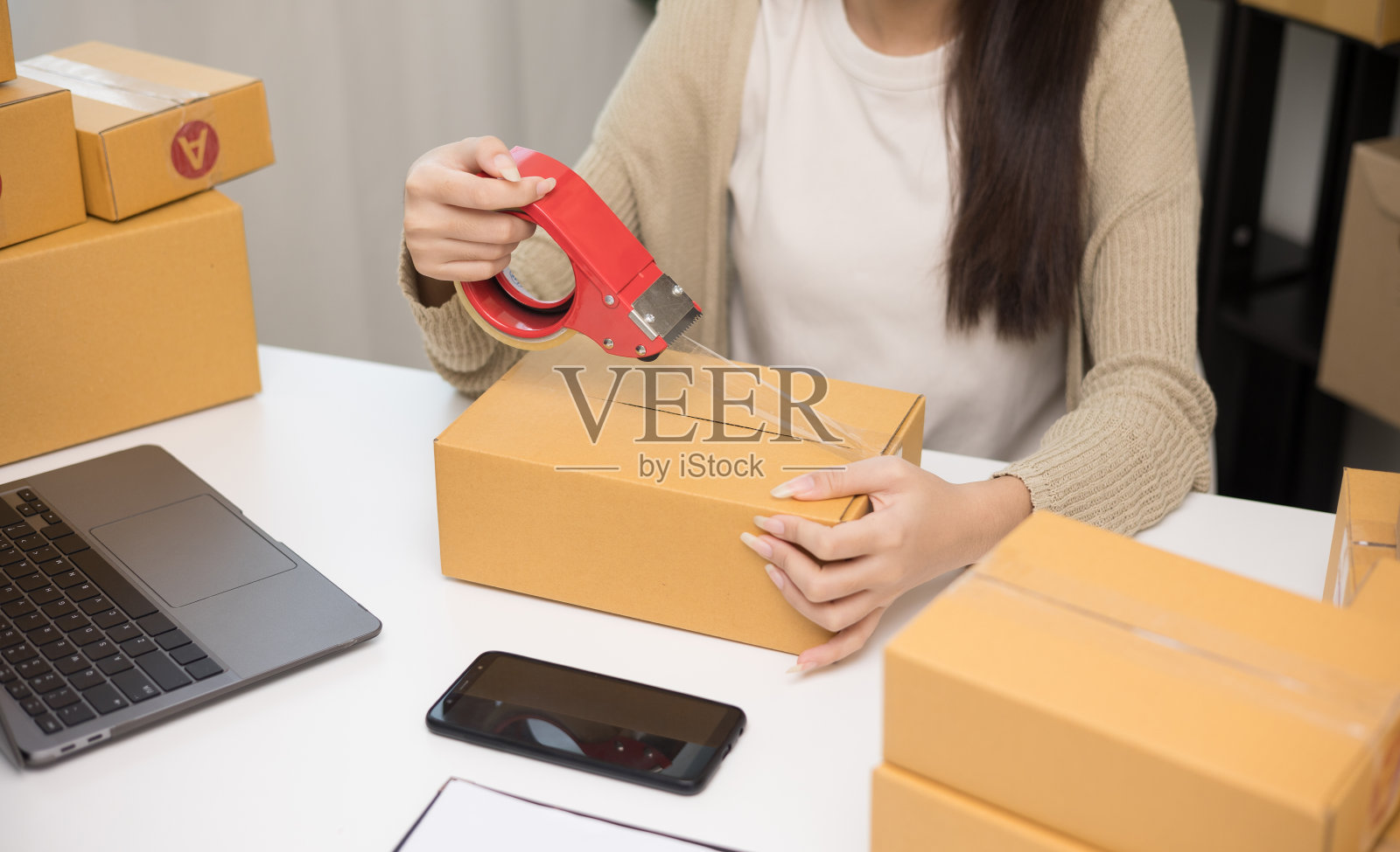 关闭女商人手包装产品密封纸板与管道胶带。小企业主企业家包装产品在盒子里照片摄影图片