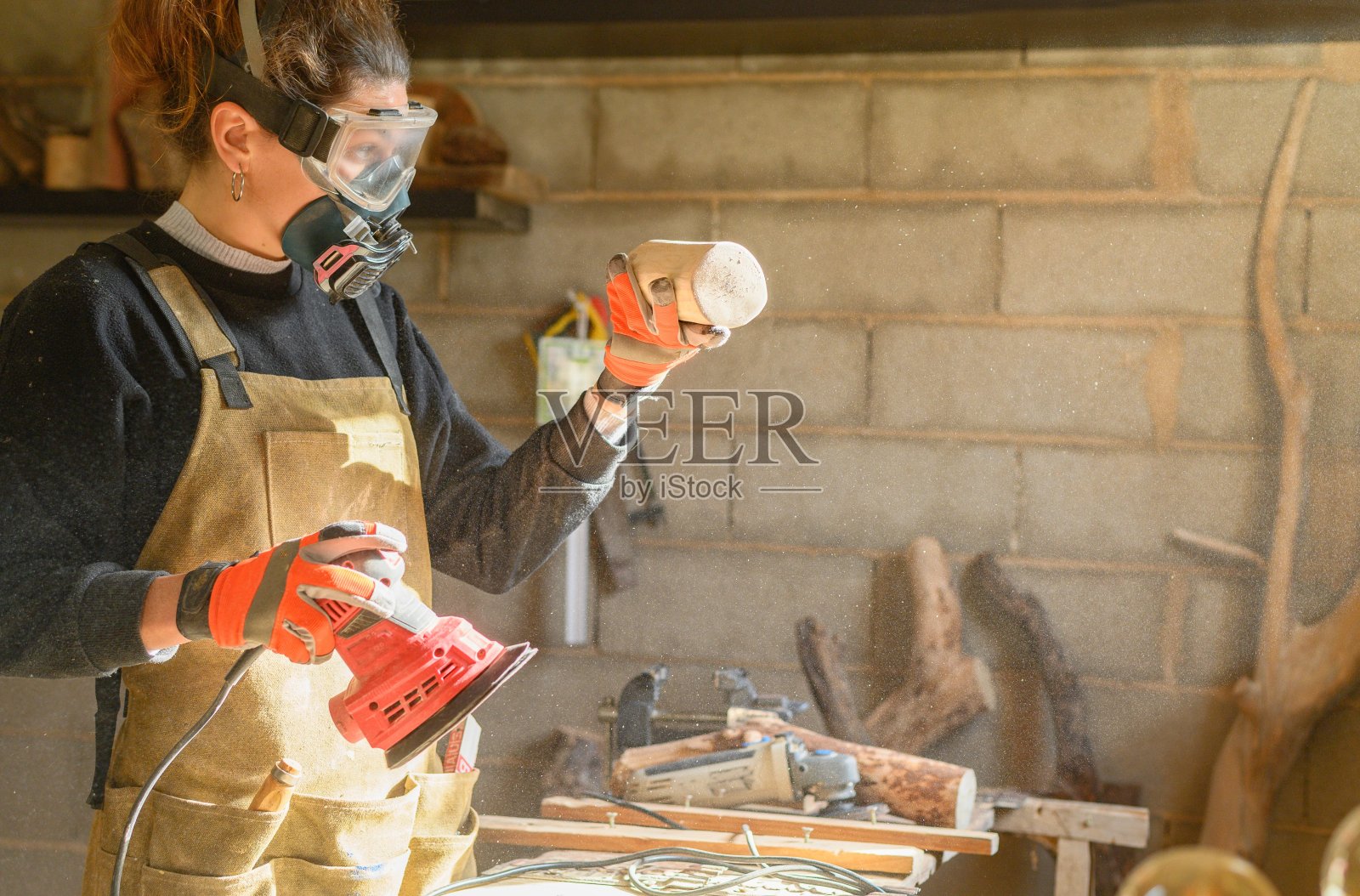 木匠女工带着面罩、护目镜和防护手套，在木工车间用打磨机检查粗木。照片摄影图片