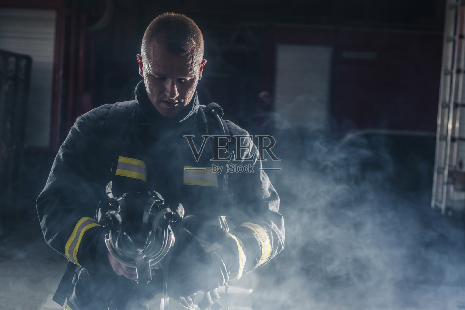 一名消防员穿着消防服和头盔的肖像。黑色背景与烟和蓝光。照片摄影图片