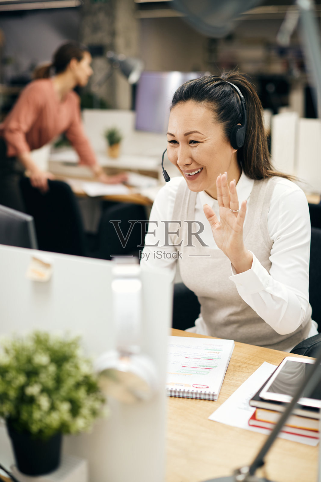 快乐的亚洲女商人欢迎某人，而有视频电话在办公室。照片摄影图片