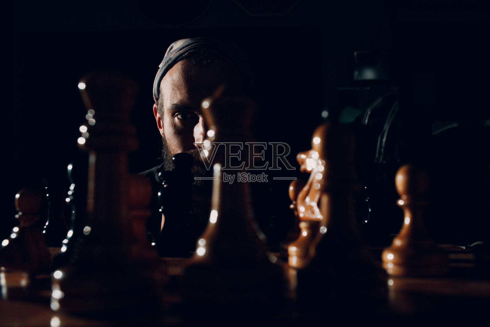 年轻的成年英俊男子下棋在黑暗与侧照明照片摄影图片