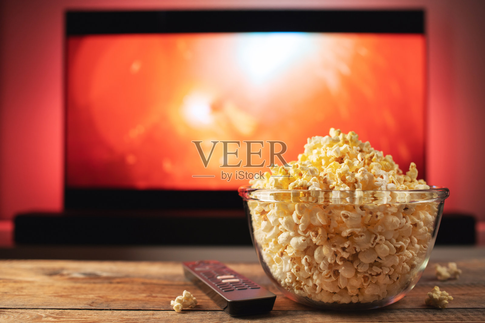 一个装着爆米花的玻璃碗和电视后台的遥控器。晚上舒适地在家看电影或电视剧照片摄影图片