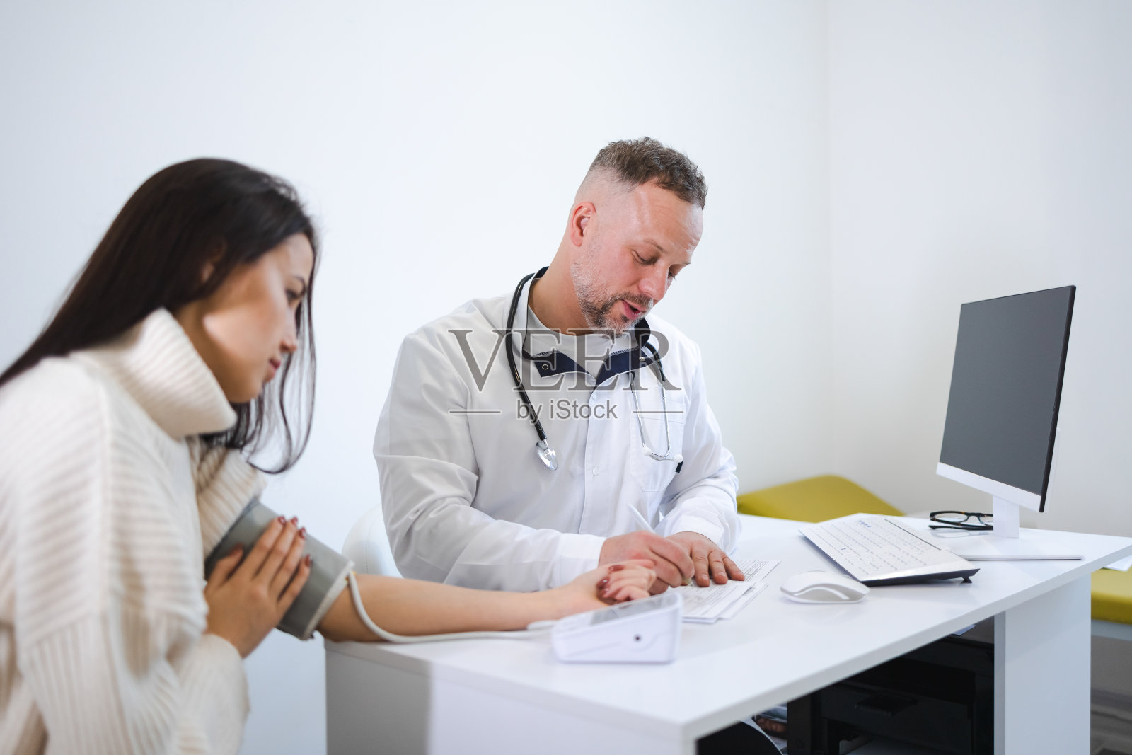 男医生测量女医生的血压，并将结果记录在病人的卡片上。女性就诊于心脏病专家照片摄影图片