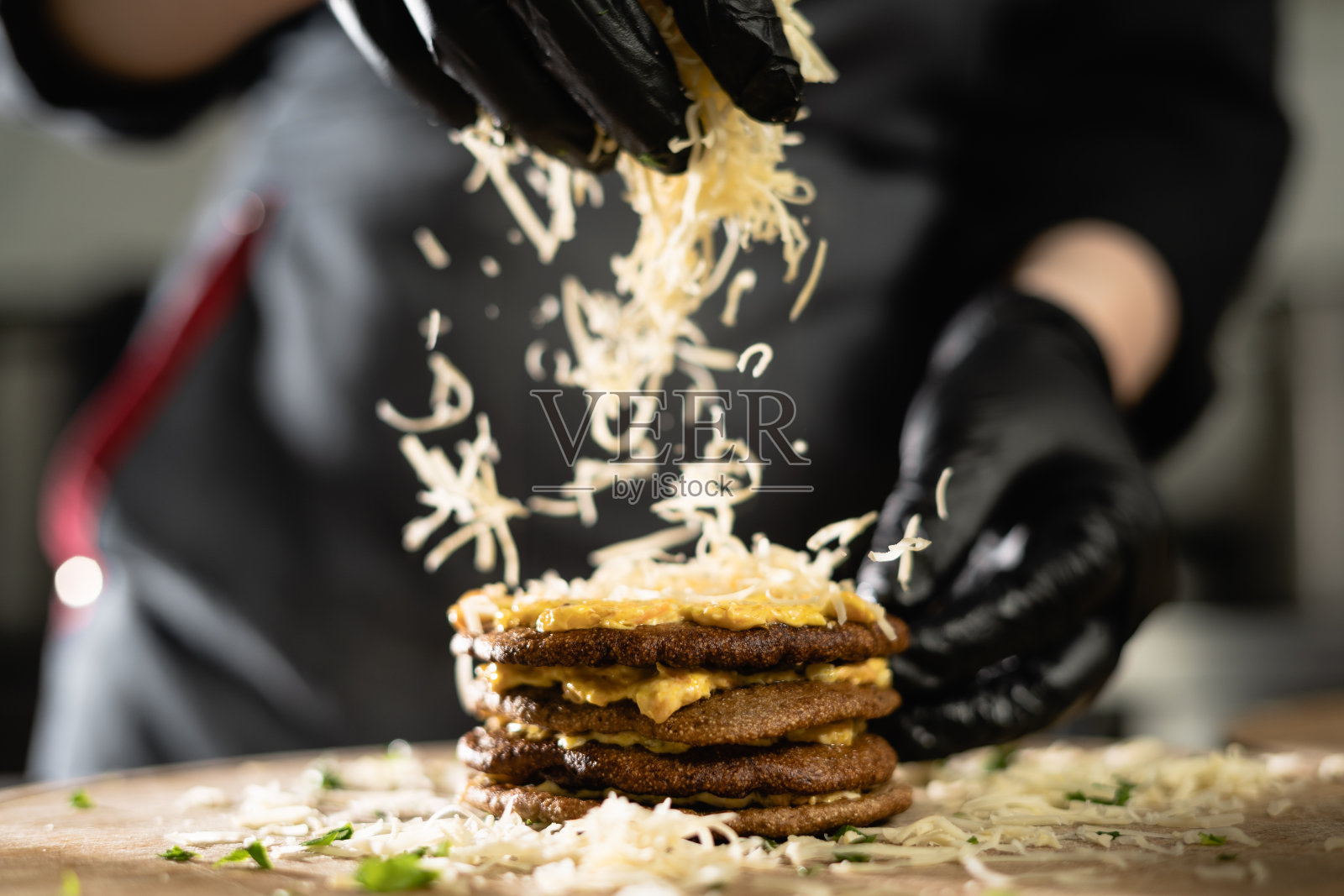 厨师在厨房里准备肝馅饼。特写的女性手在手套上撒着奶酪肝煎饼。照片摄影图片