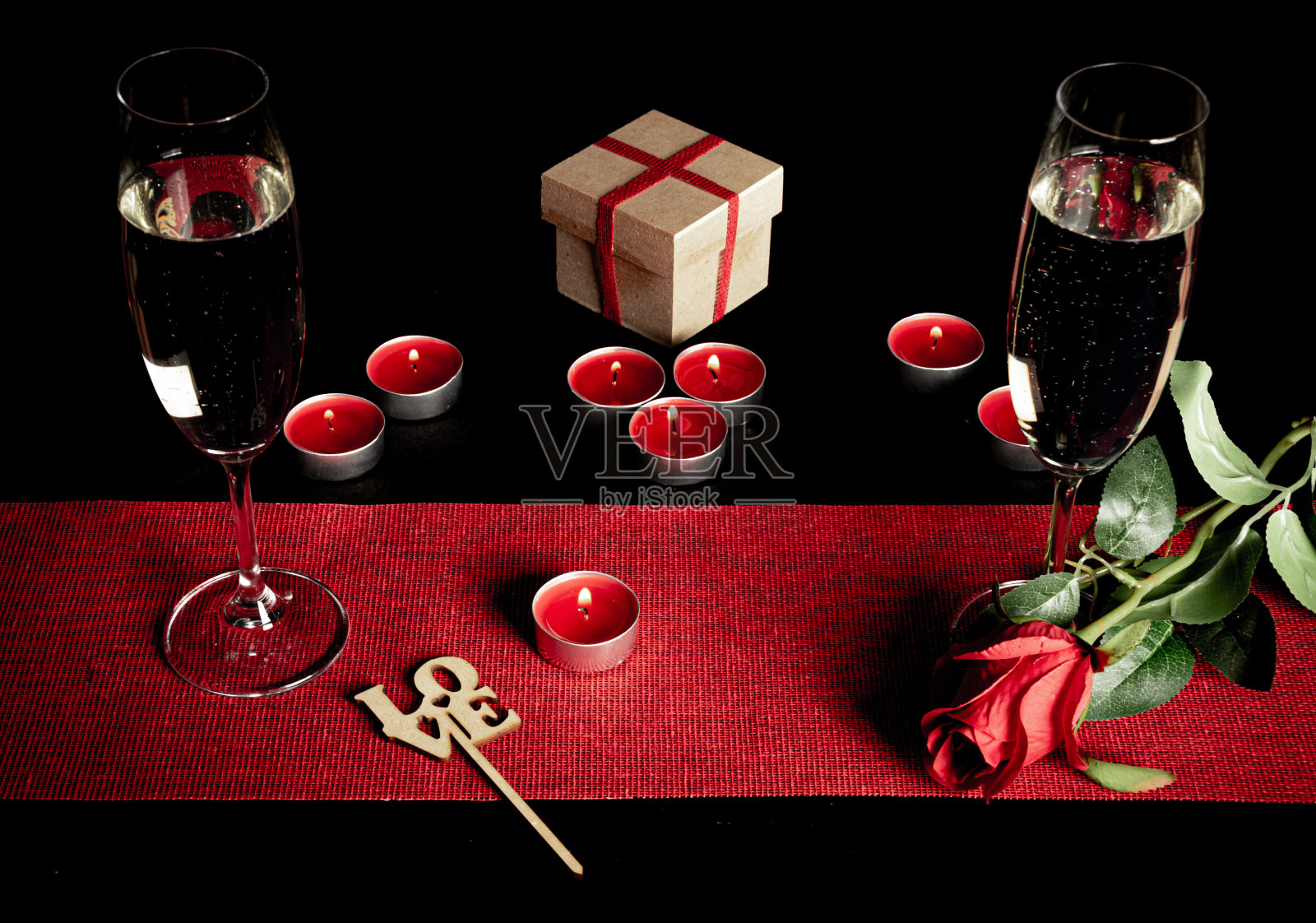 桌子上有蜡烛，两个香槟杯，一个礼品盒和一支玫瑰在黑色的背景上照片摄影图片