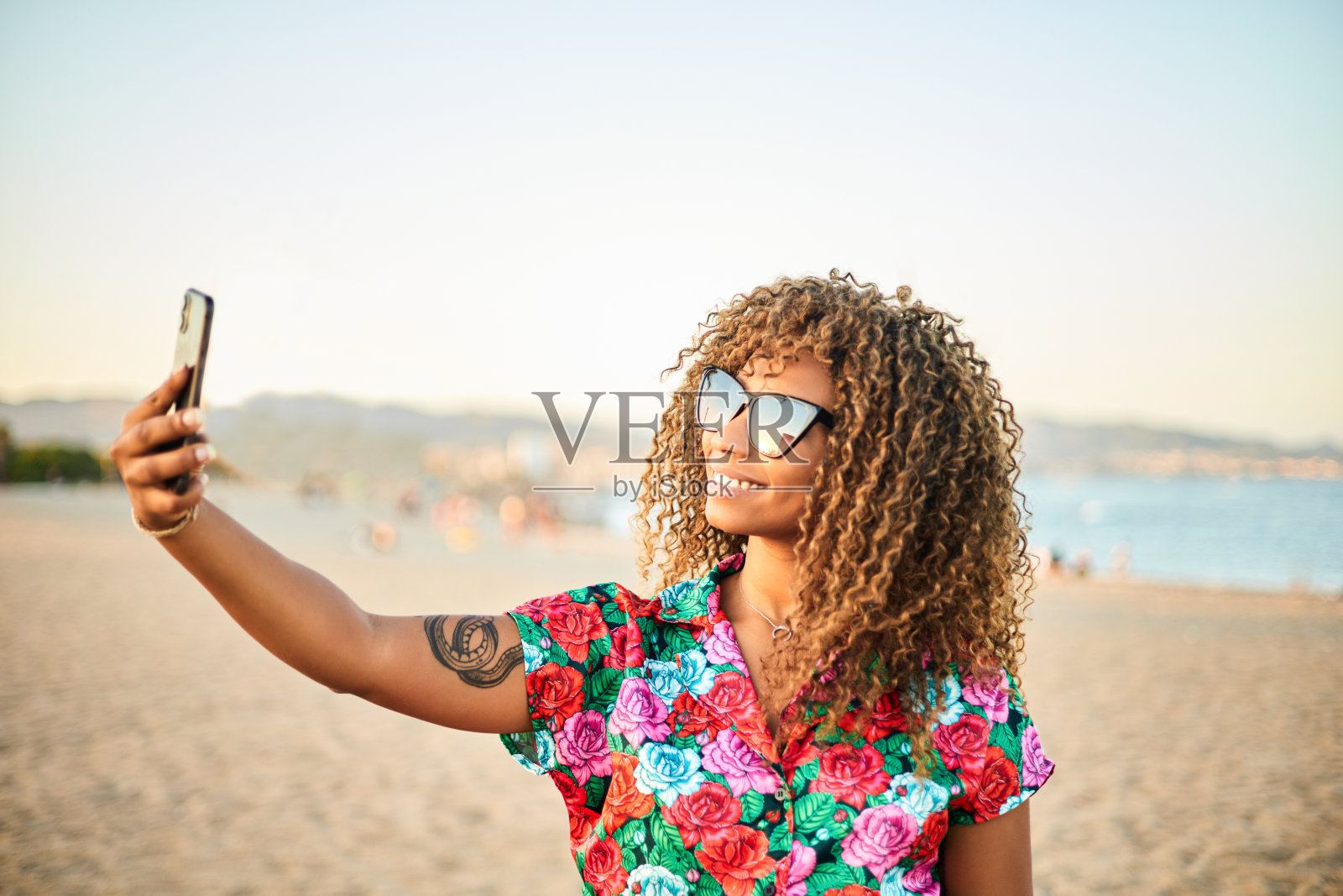 非裔美国女孩在日落时分用她的手机在海滩上自拍。照片摄影图片