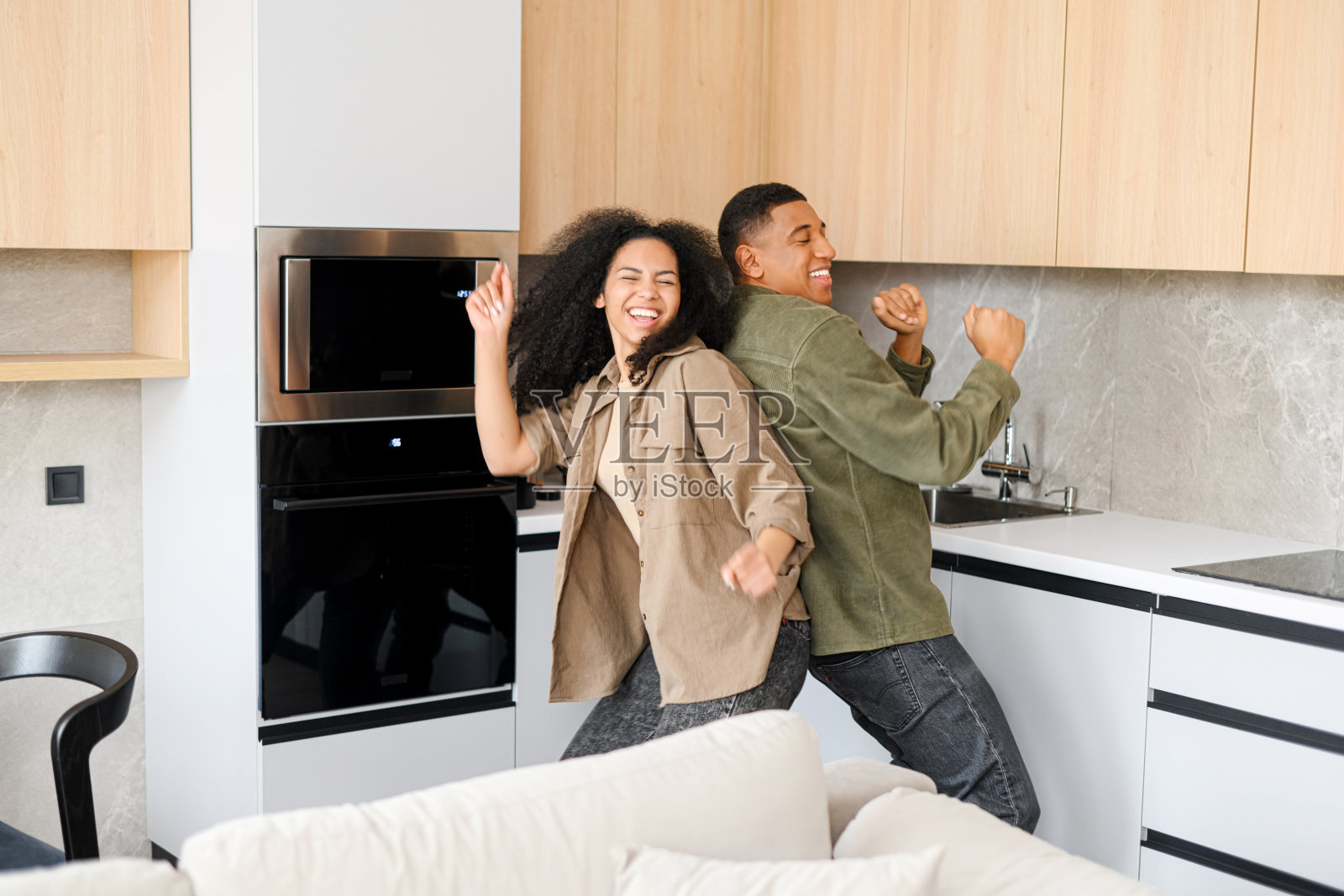 这对穿着家庭服装的年轻夫妇背靠背站在家里的厨房里跳舞的上半身人像照片摄影图片