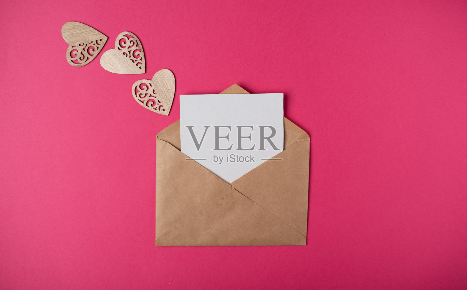 信封里面有一张空白纸和粉红色背景上的木制心。照片摄影图片