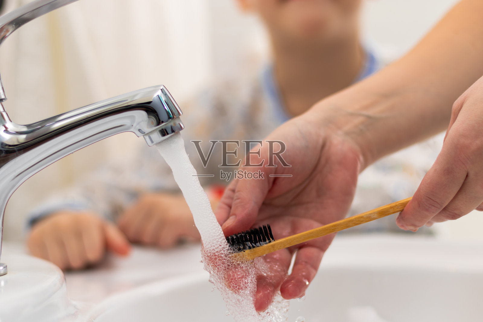 在家里的浴室里，母亲的手帮助孩子在睡前刷牙。有选择性的重点。照片摄影图片