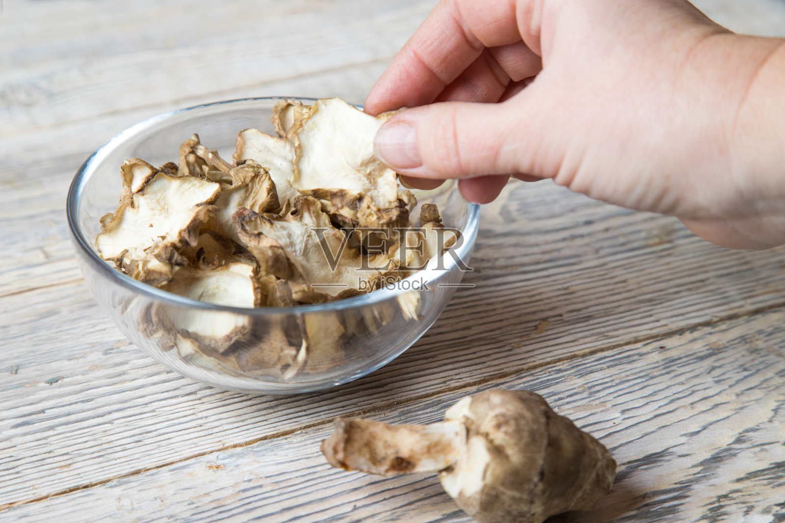 一位妇女的手放在一个浅木色背景上放着干菊芋片的盘子上。照片摄影图片