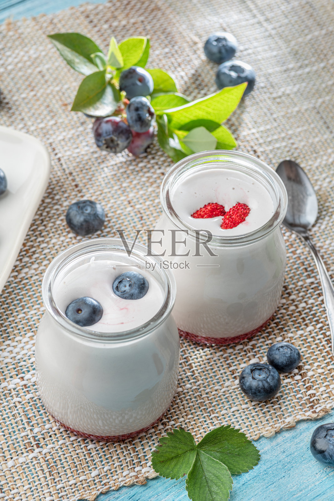 桌上放着两个装着原味酸奶和浆果的玻璃容器。夏天的心情。照片摄影图片