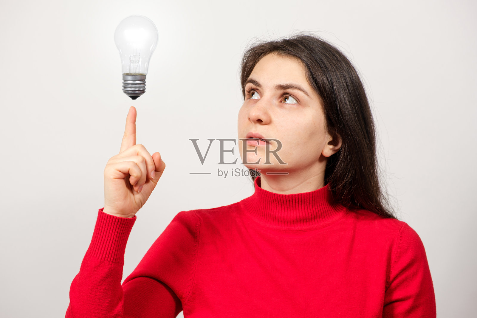 一名女子抬起头，用手指着一个发光的灯泡。照片摄影图片