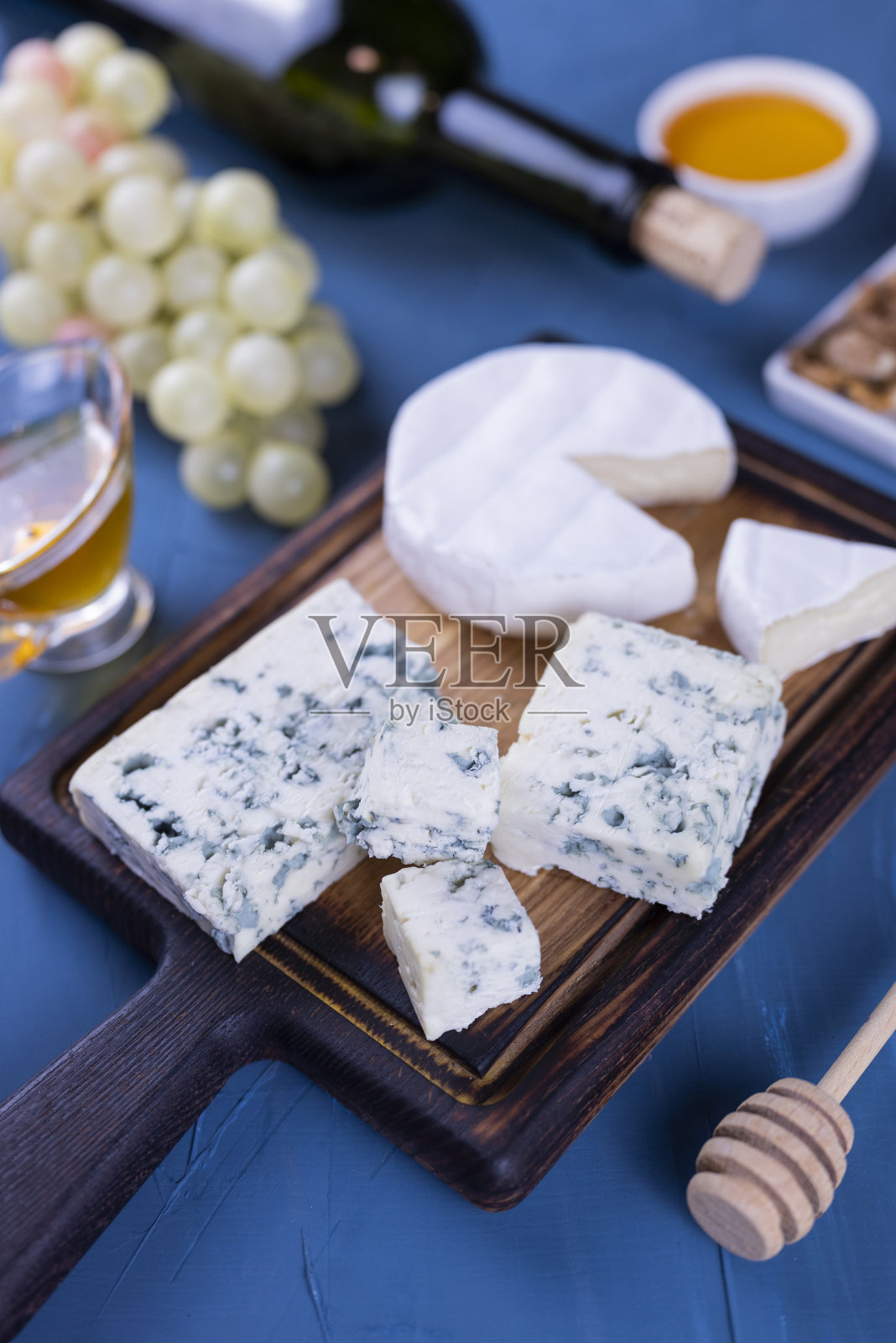开胃菜搭配蓝色奶酪和卡门培尔奶酪放在木板上，配上蜂蜜、葡萄和一瓶葡萄酒照片摄影图片