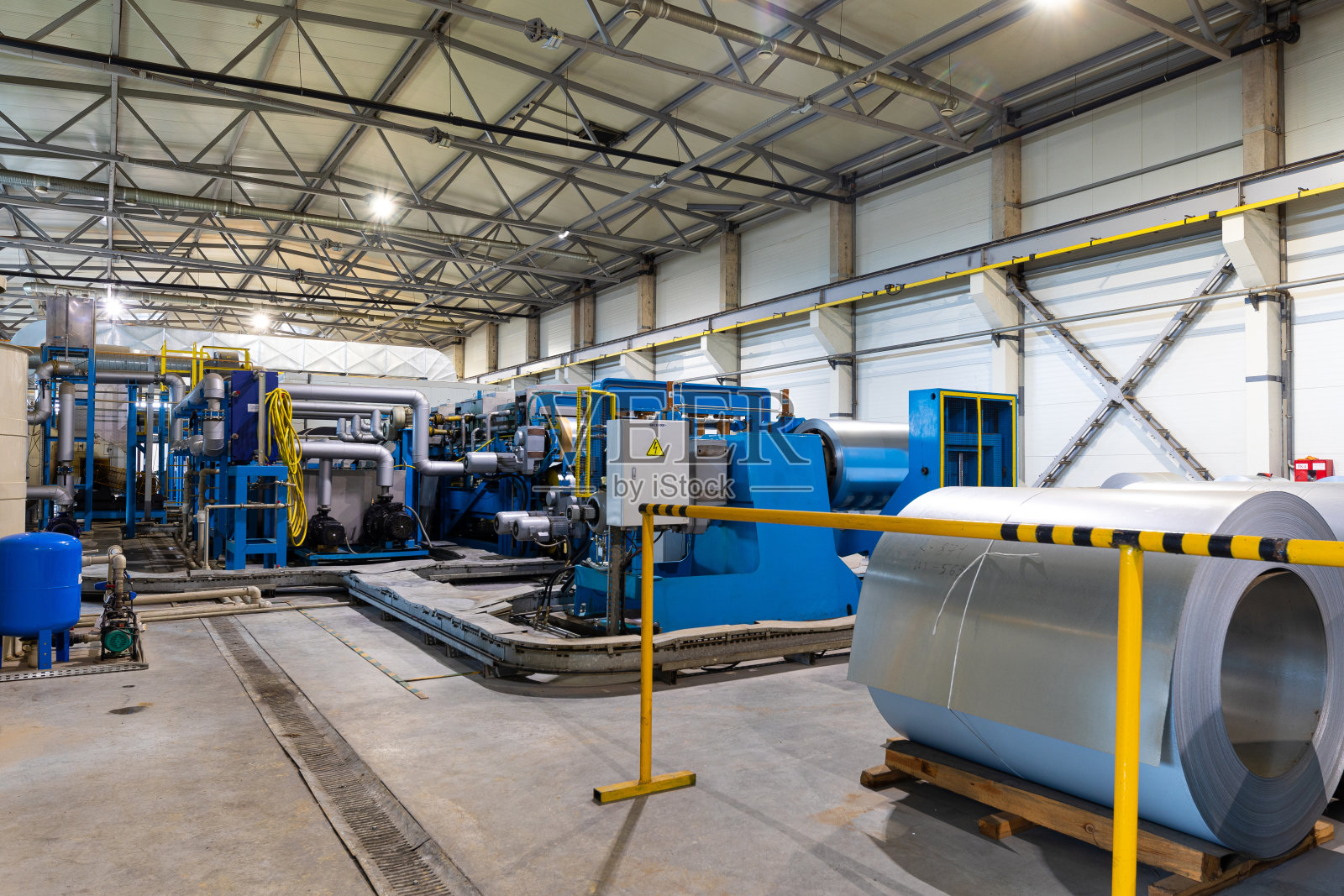 屋顶金属瓦生产线照片。金属车间的成型机。金属板材仿形机。背景的植物照片摄影图片