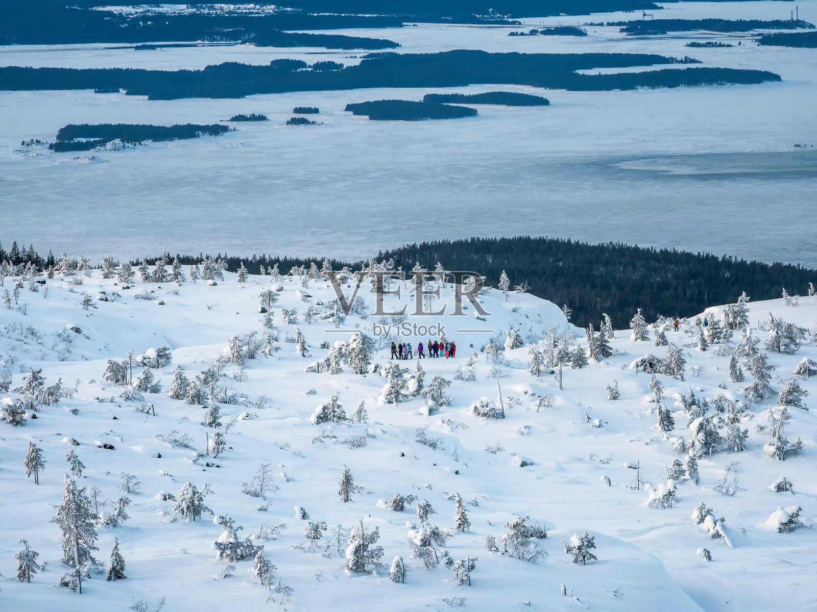 一群游客的小剪影，在冰雪覆盖的奇花异草和地平线上的一群岛屿之间的雪山山顶。冬季徒步旅行，旅游理念。照片摄影图片