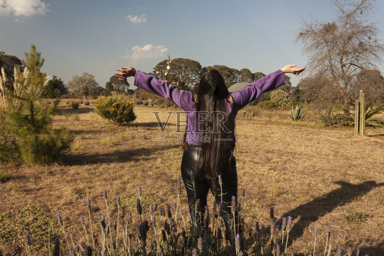 另一种穿着皮裤和紫色脱肩毛衣的女人伸展着她的手臂，在乡村中央旋转照片摄影图片