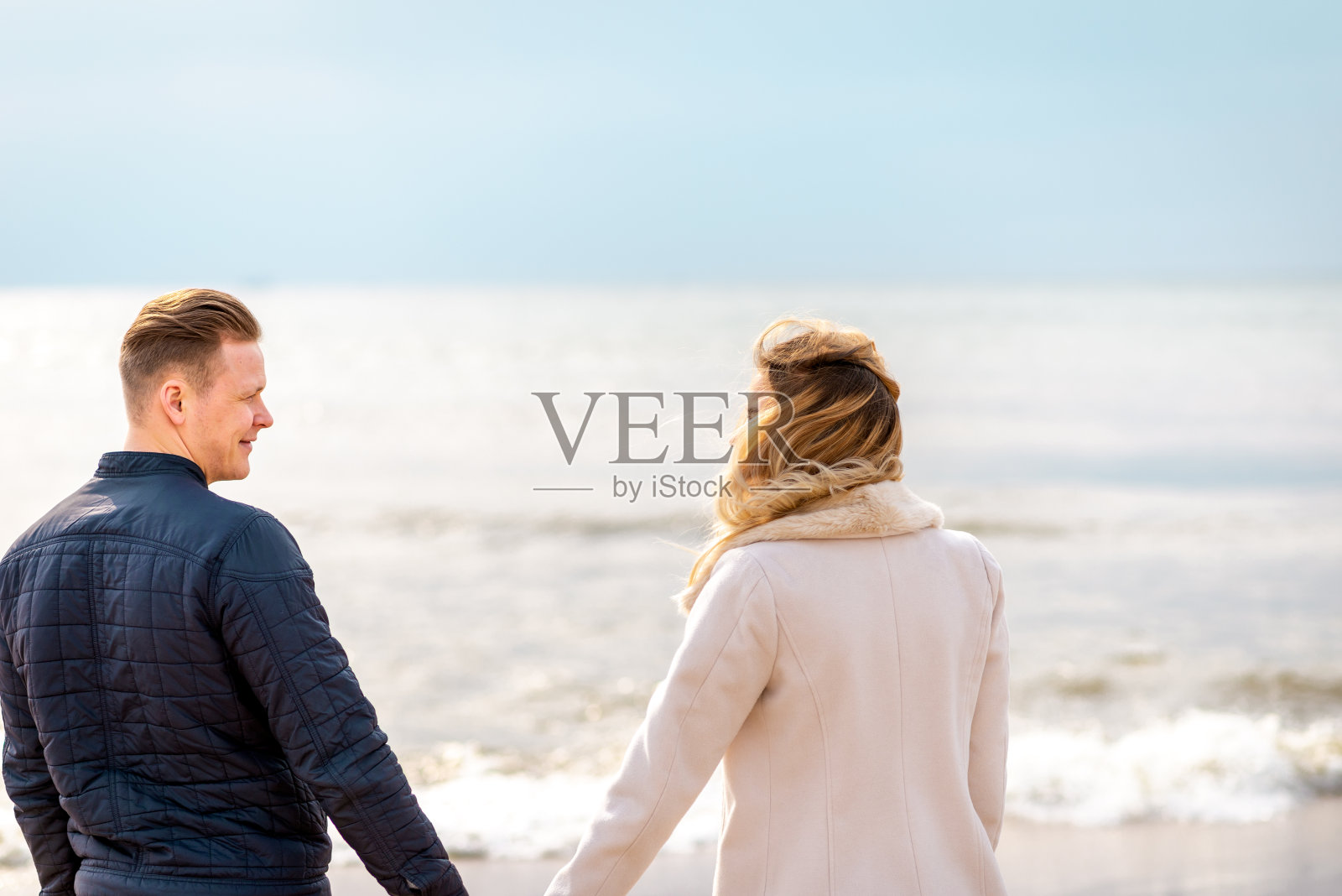 沙滩上的一对手牵着手夕阳西下。浪漫的年轻夫妇享受阳光，阳光，夫妇在春假。照片摄影图片