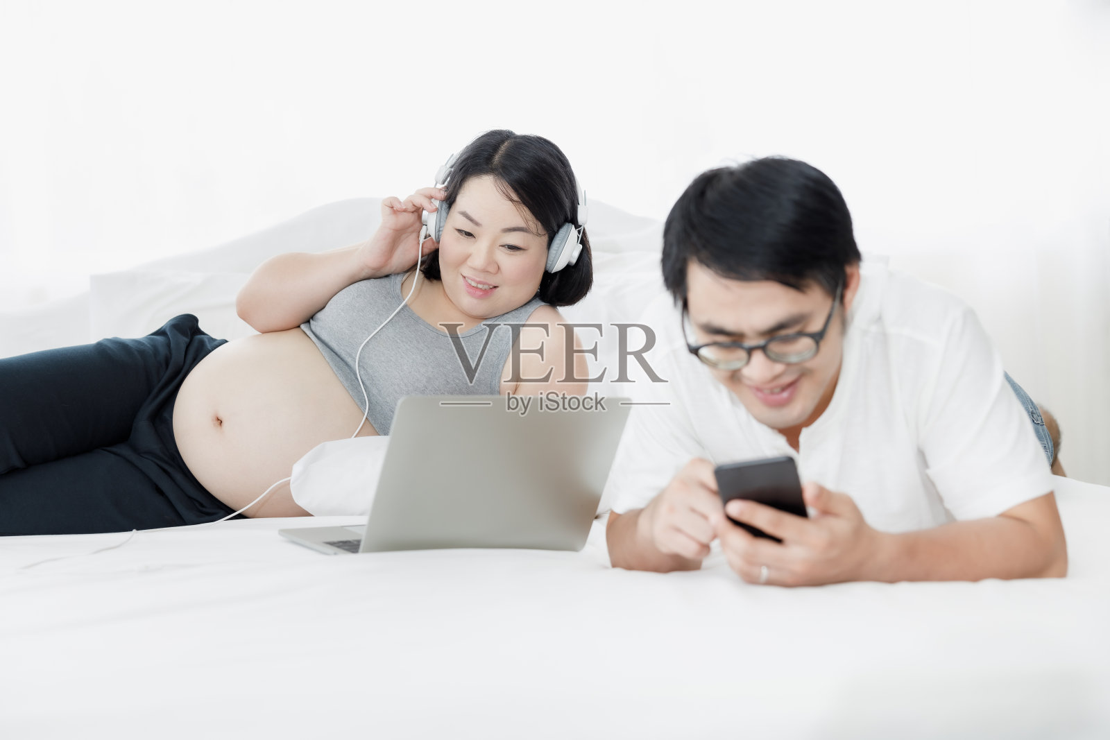 亚洲孕妇和丈夫躺着放松听音乐玩手机照片摄影图片