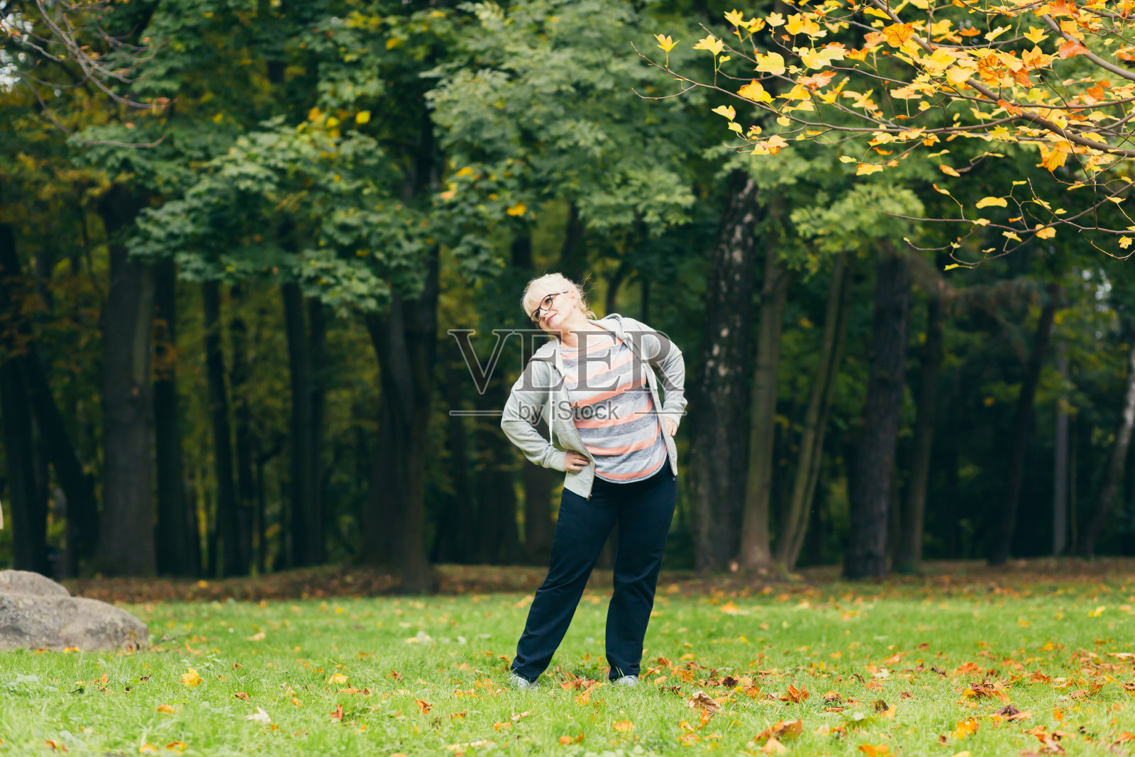老年妇女站在公园的草地上做运动，锻炼身体，过着健康积极的生活方式照片摄影图片