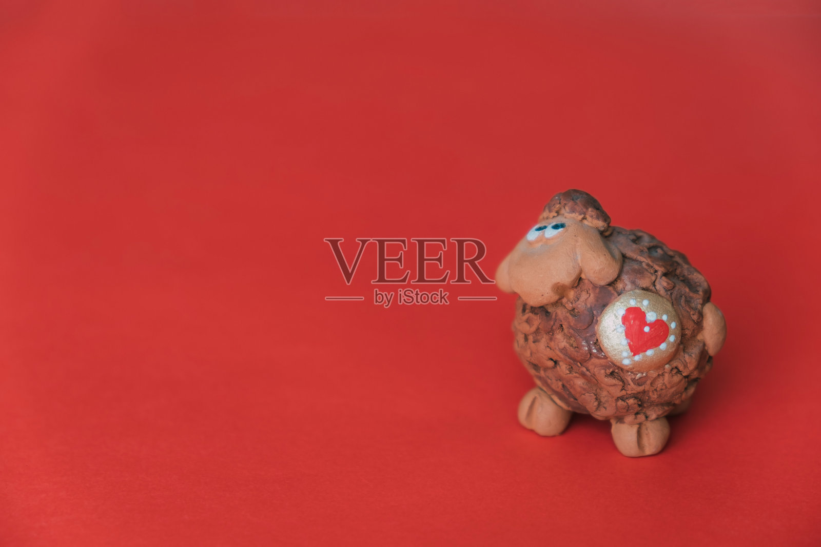 红色背景上有一颗心的泥人羊。照片摄影图片