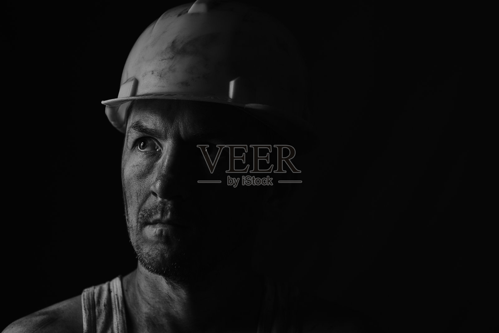 煤矿工人肮脏的脸在黑色的背景上。头戴安全帽的疲惫矿工。黑白相片肖像。照片摄影图片