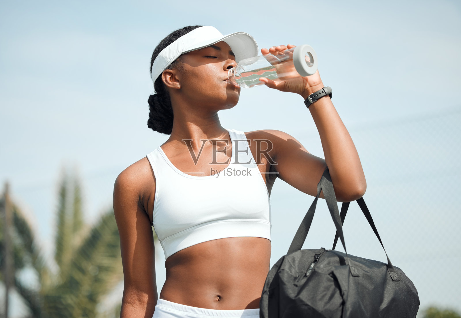 这张照片拍摄的是一名运动的年轻女子在户外打网球时喝水照片摄影图片