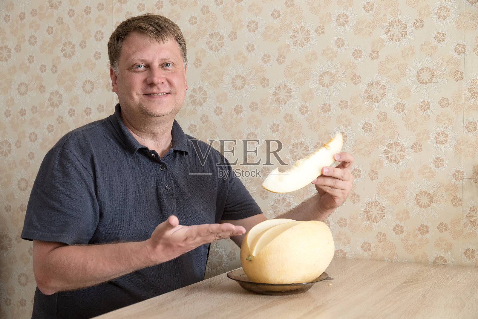 坐在桌旁的一位热情好客的成年金发男子邀请你品尝甜瓜照片摄影图片