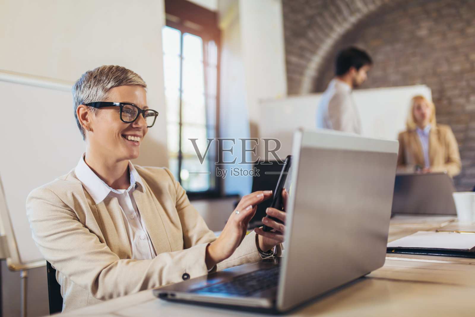 快乐的女商人使用笔记本电脑和手机与团队讨论项目的背景。照片摄影图片