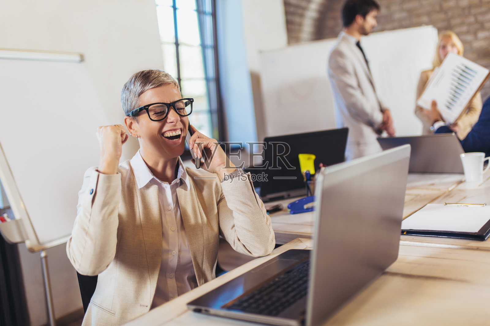 快乐的女商人使用笔记本电脑和手机与团队讨论项目的背景。照片摄影图片