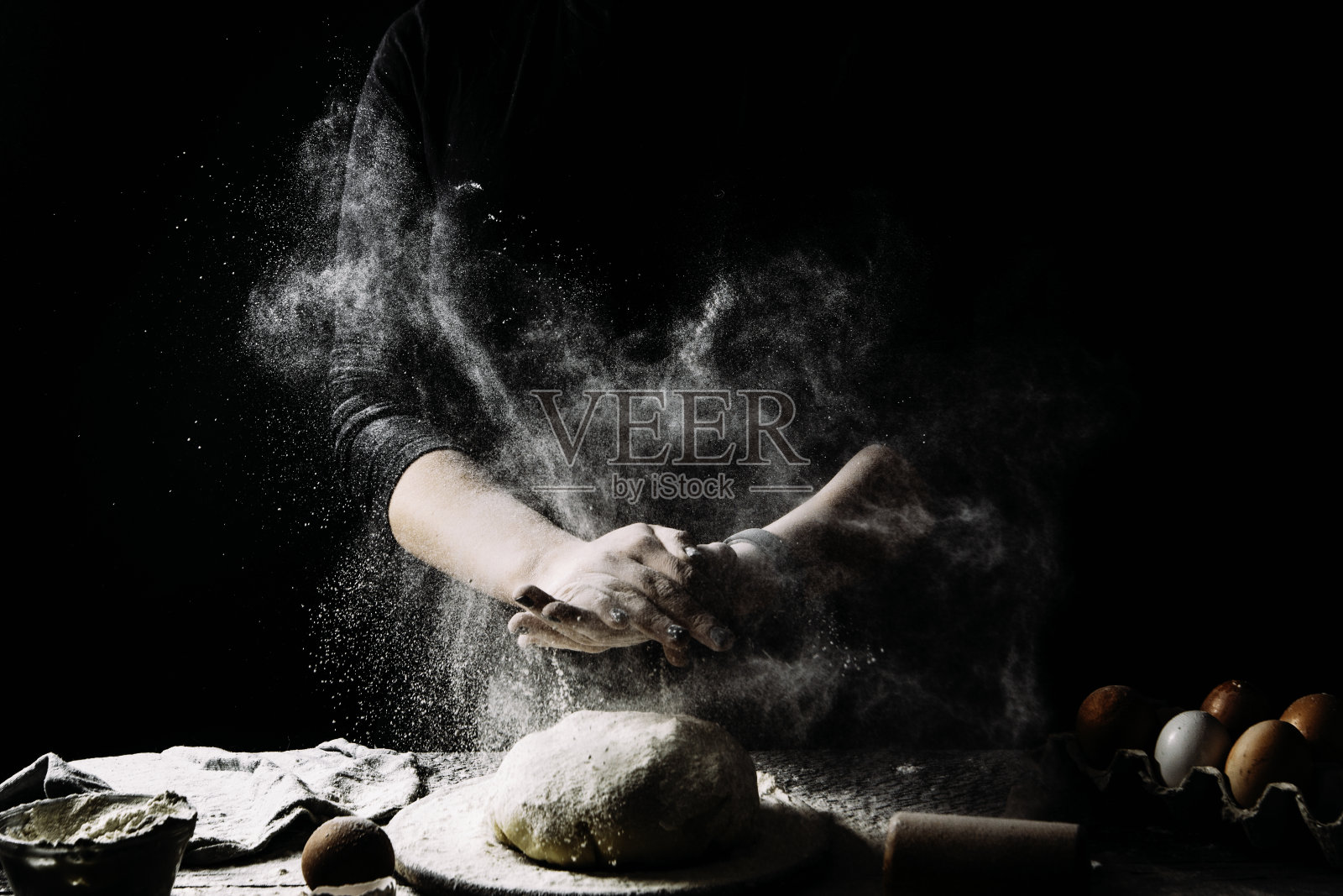 在面包店或家里用手揉面团。空气中弥漫着面粉。女厨师准备在桌子上揉面，撒面粉的手的特写照片摄影图片