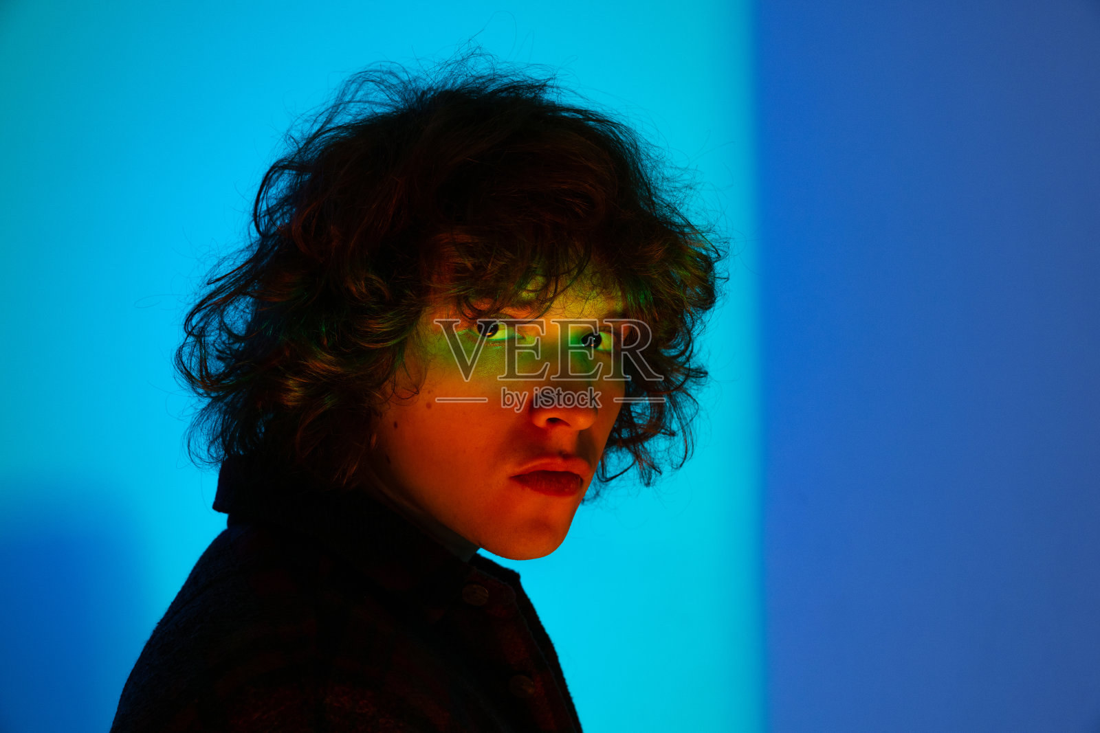 一个悲伤的人的特写脸，学生看着镜头孤立在蓝色的背景霓虹灯。情感观念、学习观念、教育观念、时尚观念照片摄影图片