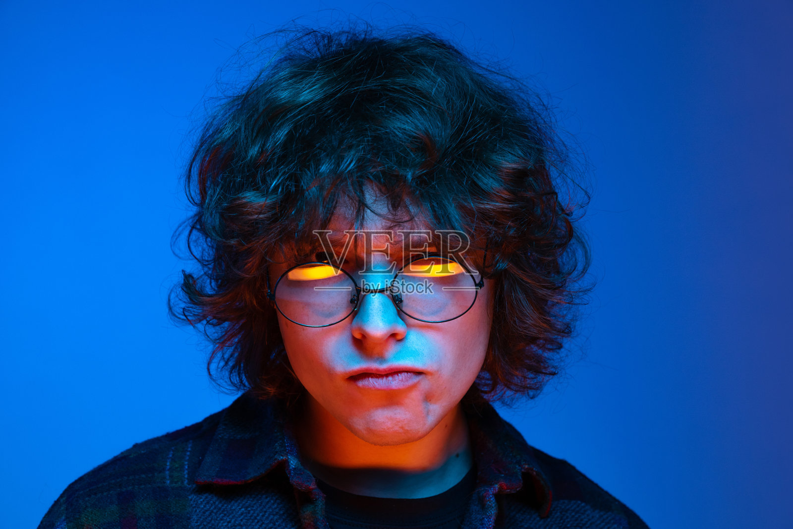 一个悲伤的人的特写脸，学生看着镜头孤立在蓝色的背景霓虹灯。情感观念、学习观念、教育观念、时尚观念照片摄影图片
