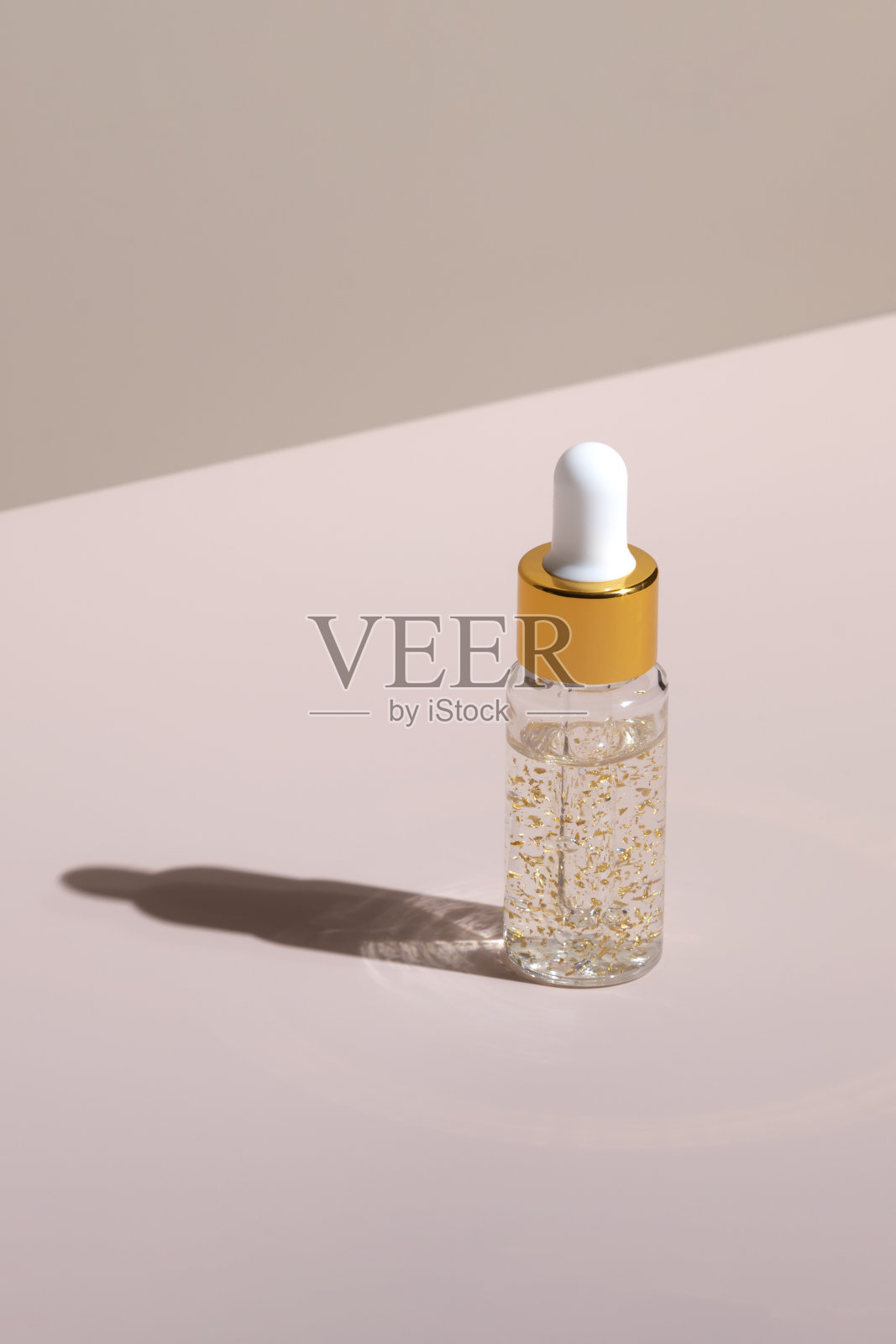 天然皮肤护理化妆品在滴管瓶金色血清与硬阴影在柔和的中性粉红色背景垂直布局照片摄影图片