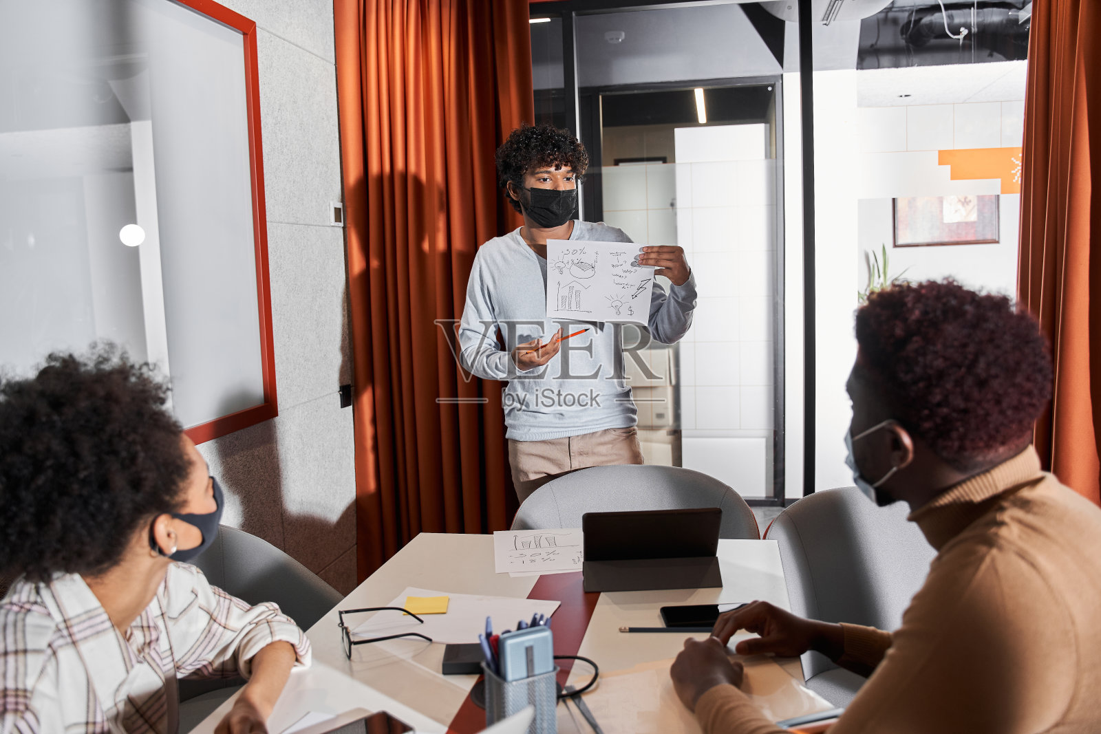 员工们坐在会议室里，而戴着防护口罩的人正在展示计划照片摄影图片