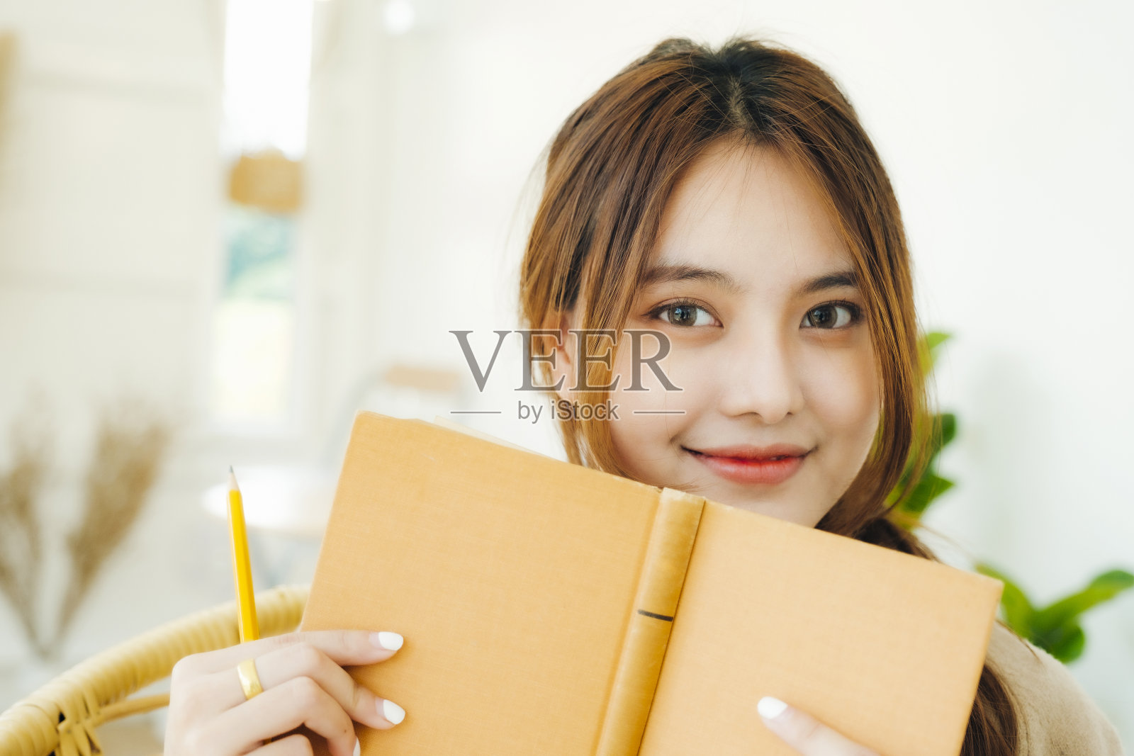 一名年轻女学生的肖像用一本黄色的书遮住了她的脸照片摄影图片